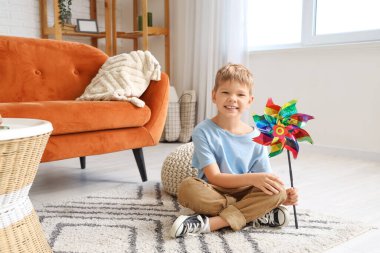 Oyuncak yel değirmenli şirin bir çocuk evde oturuyor.