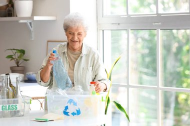 Mutfaktaki masasında çöp konteynırı olan yaşlı bir kadın. Atık sıralama kavramı
