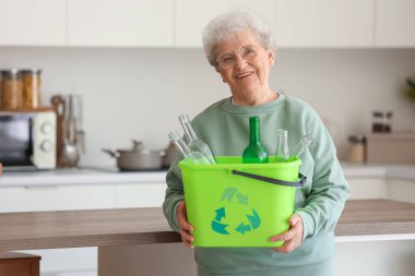 Mutfakta çöp tenekesi olan yaşlı bir kadın. Atık sıralama kavramı