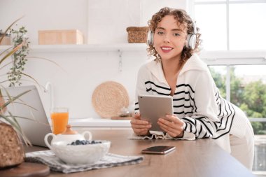 Mutfakta kulaklığı ve tablet bilgisayarı olan genç bir kadın var.