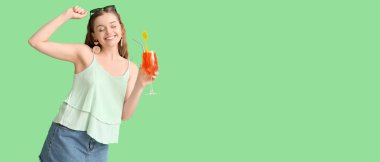 Güzel, mutlu, genç bir kadın yeşil arka planda bir bardak lezzetli aperol spreyi tutuyor.