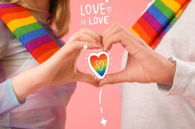 LGBT bayraklı genç bir çift pembe arka planda kalp yapıyor, yakın plan.