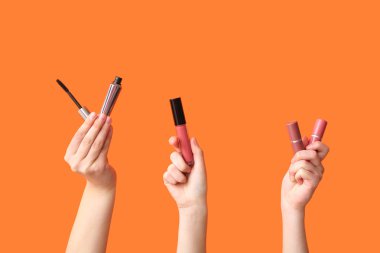 Maskara sürmüş kadın elleri ve turuncu arka planda ruj izleri.