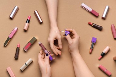 Kahverengi arka planda farklı ruj izleri olan kadın elleri.