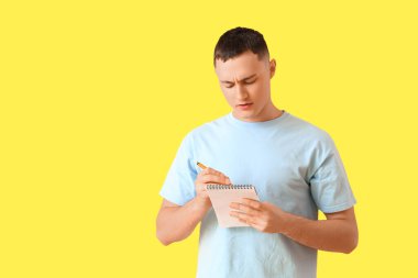 Sarı arka planda not defterine yazan genç adam. Hatırlatma konsepti