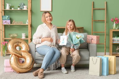 Güzel genç bir kadın ve bir buket lale, çizim ve hava balonu olan küçük tatlı kızı oturma odasındaki kanepede oturuyor.