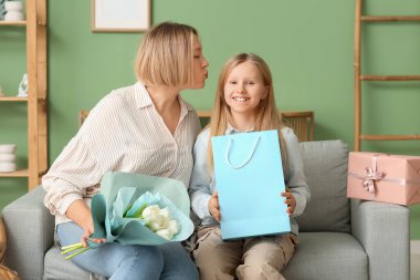 Elinde lale buketi tutan genç ve güzel bir kadın ve oturma odasındaki kanepede oturan küçük tatlı kızı.