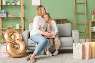 Güzel genç bir kadın ve hediye kutusu ve hava balonu olan sevimli küçük kızı oturma odasındaki kanepede oturuyor.
