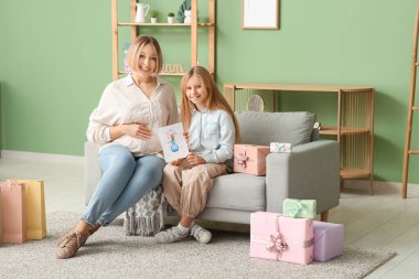 Güzel genç bir kadın ve küçük tatlı kızı oturma odasındaki kanepede oturmuş hediye kutuları çiziyorlar.