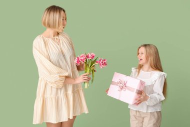 Güzel genç bir kadın elinde lale buketi ve yeşil arka planda hediye kutusuyla küçük tatlı bir kız tutuyor.