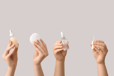 Beyaz arka planda pipet ve pamuk pedlerle tırnak eti yağı şişelerini tutan kadın eller