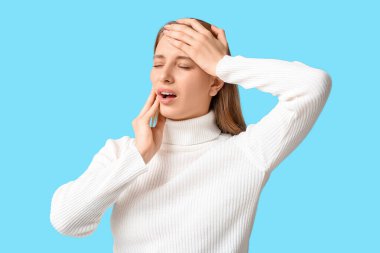 Mavi arka planda diş ağrısından muzdarip güzel genç bir kadın.