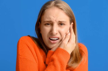 Mavi arka planda diş ağrısından muzdarip güzel genç bir kadın.