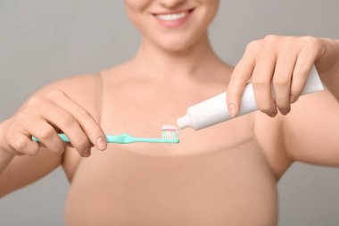 Gri arka planda diş fırçası ve tutkal tüpüyle güzel, genç, mutlu bir kadın. Yakın plan.