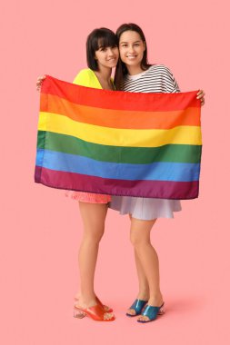 Pembe arka planda LGBT bayrağı olan genç lezbiyen çift