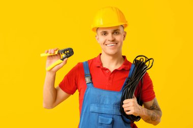 Sarı arka planda kablo ve tel tutacağı olan genç bir elektrikçi.