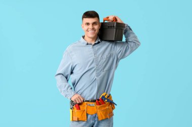 Mavi arka planda alet çantası ve kemeri olan genç bir elektrikçi.