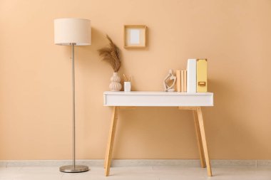 Masası, kitapları ve bej duvarın yanında lambası olan şık bir iş yeri.