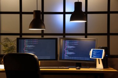 Geceleri karanlık ofiste bilgisayar monitörlü ve tabletli programcı masası.