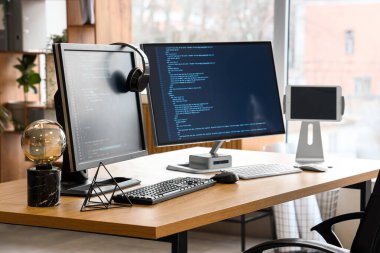Ofisteki masada programlama kodlu ve kulaklıklı bilgisayar monitörleri