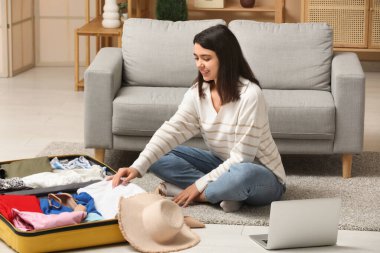 Gülümseyen genç bir kadın şık bir oturma odasında bavullarını hazırlıyor.