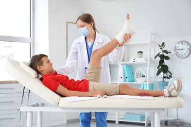 Female doctor examining little boy's bandaged foot in clinic