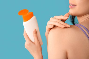 Genç bir kadın mavi arka planda omzuna güneş kremi sürüyor. Yakın çekim.