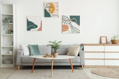 Modern interior of living room with grey sofa, chest of drawers and houseplant on table
