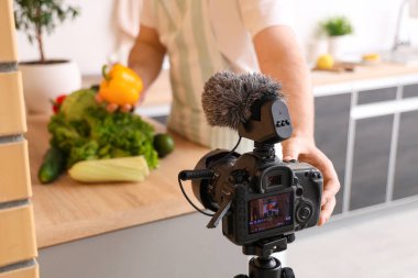 Mutfakta taze sebzeleri olan genç bir adamı kaydeden profesyonel video kameraya yakın çekim.