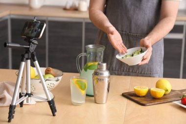 Genç adam onun mutfakta ev yapımı limonata yaptığını videoya kaydediyor.