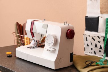 Bej arka planda terzi malzemesi olan modern dikiş makinesi.