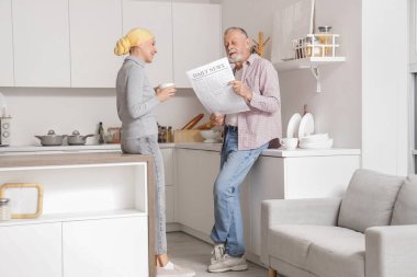 Kemoterapiden sonra bir fincan kahveyle yetişkin bir kadın ve kocası mutfakta gazete okuyor.