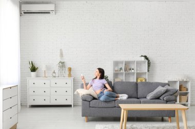 Evdeki kanepede oturan klimalı uzaktan kumandalı güzel bir genç kadın.