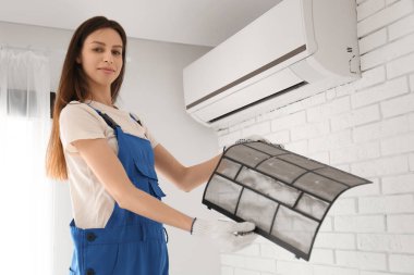 Kadın teknisyen evde kirli klima filtresi değiştiriyor.