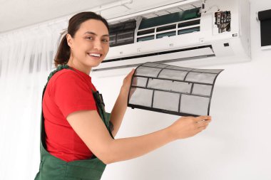 Kadın teknisyen evde kirli klima filtresi değiştiriyor.