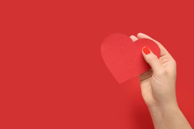 Kırmızı manikürlü kadın eli ve arka planda kağıt kalp. Sevgililer Günü kutlaması
