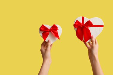 Sarı arka planda kalp şeklinde hediye kutuları olan kadın eller. Sevgililer Günü kutlaması