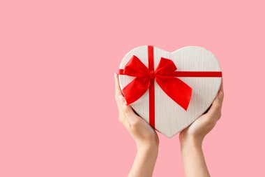 Pembe arka planda kalp şeklinde hediye kutusu olan kadın elleri. Sevgililer Günü kutlaması