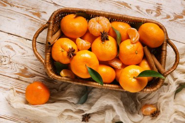 Beyaz ahşap zemin üzerinde yıldız anason ve tarçın olan sepet dolusu tatlı mandalina.