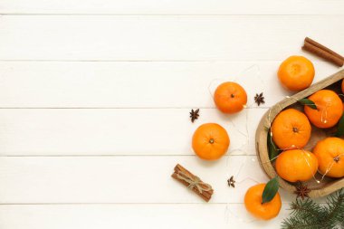 Noel ışıkları parlayan bir tepsi tatlı mandalina ve beyaz ahşap arka planda tarçın