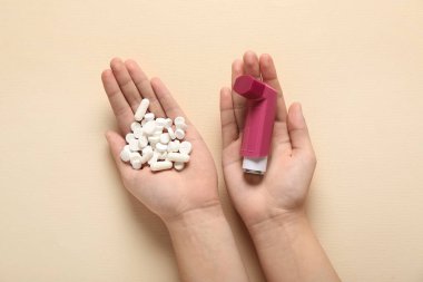 Astım spreyli çocuk elleri ve bej arka planda haplar.