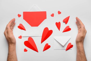 Zarflı erkek eller, boş kart ve beyaz arka planda kırmızı kağıt kalpler. Sevgililer Günü kutlaması