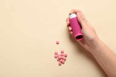 Astım spreyli çocuk eli ve bej arka planda haplar.