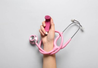Astım spreyi ve beyaz arka planda steteskop olan bir çocuk eli.