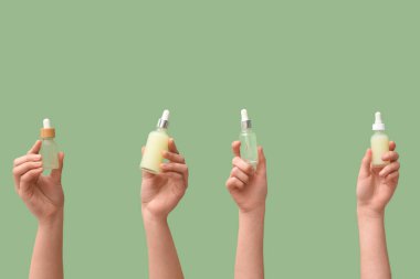 Yeşil arka planda farklı kozmetik yağı şişeleri olan kadın eller.