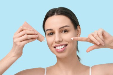 Mavi arka planda yüz kremi tüpü olan güzel genç bir kadın.