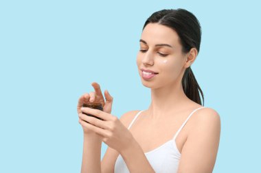 Mavi arka planda yüz kremi kavanozu olan güzel genç bir kadın.