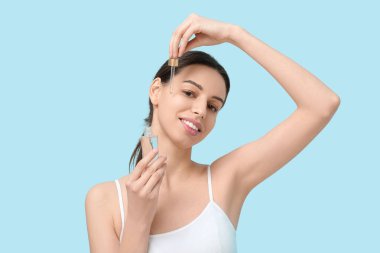 Pipetli güzel genç bir kadın mavi arka planda yüz serumu uyguluyor.