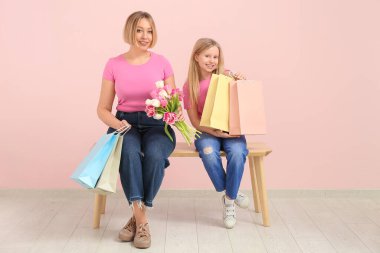 Bir buket lale ve elinde kese kâğıdıyla pembe duvarın yanındaki bankta oturan küçük tatlı kızıyla güzel bir genç kadın.