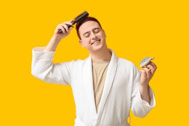 Saç derisi masajcısı ve sarı arka planda fırçası olan mutlu genç bir adam.